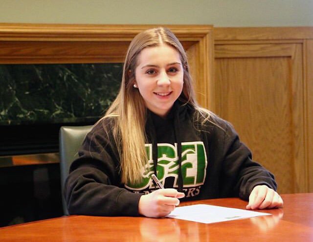 A smiling student signs a piece of paper