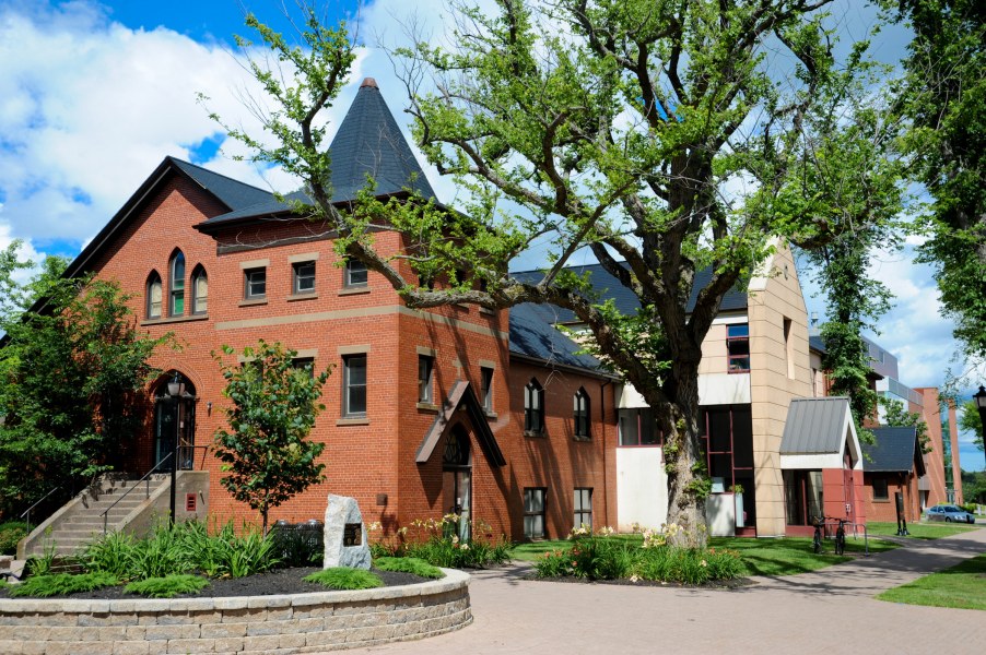 A building with mixed styles with an older section in red brick and stone and a newer section in stucco and glass