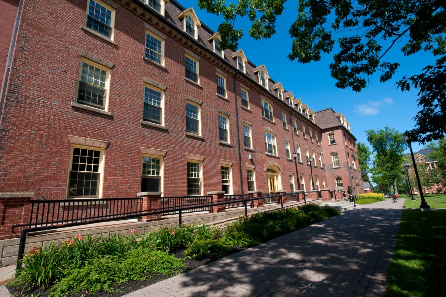 A three story old brick building framed by large trees, recognizable as UPEI's iconic SDU Main Building