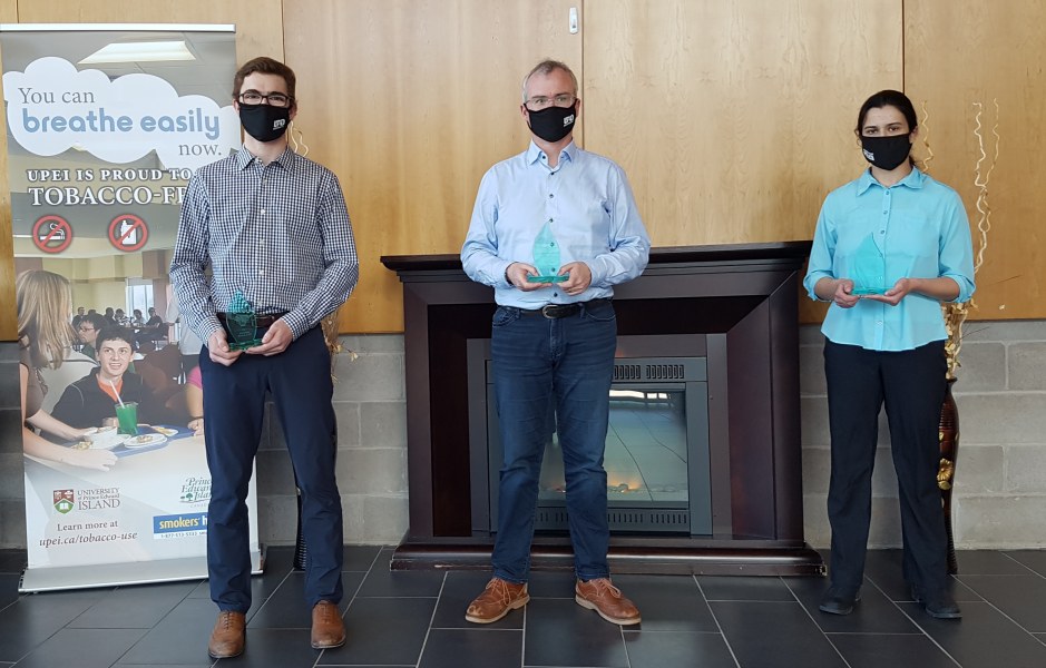 Two men and a woman stand in a line, spaced out for social distancing, wearing masks. 