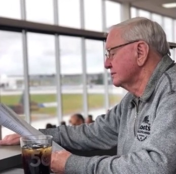 Image of Billy Mulligan seated at a table with a beverage reading a harness racing program 