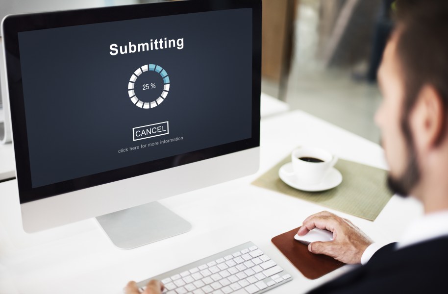 Photo of man sitting at a desk in front of a computer submitting an online form