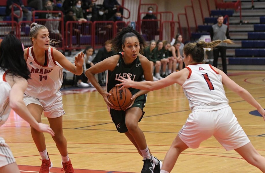 A femal baksetball player in green Panthers gear charges towards the basket in a game