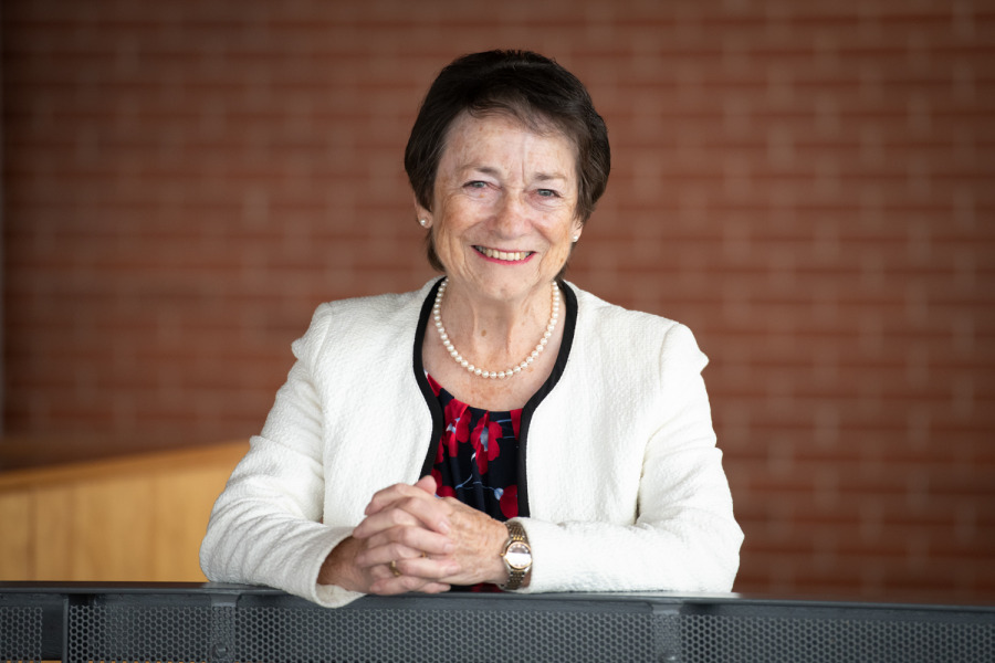 Photo of woman smiling leaning against railing with hands clasped