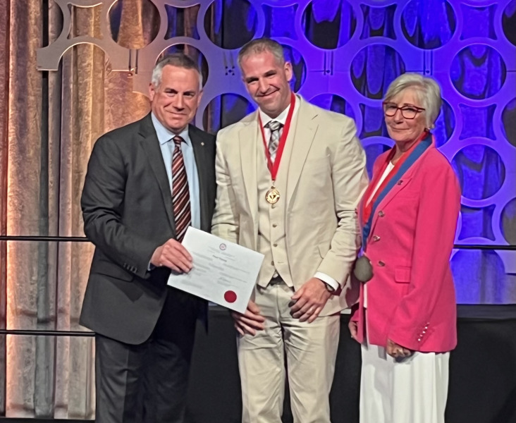 Photo of two people presenting a man with a certificate and medal