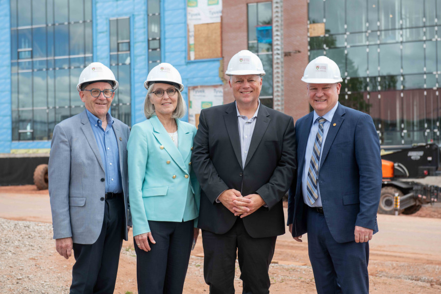 Photo of four people wearing hard hats standing in front of a building under construction