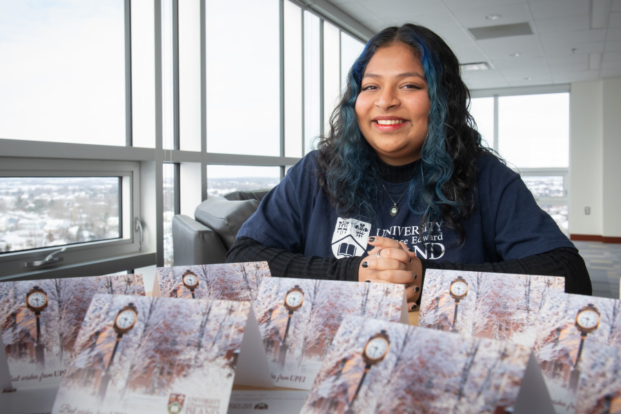 Prisha Halder, senior residence life advisor at UPEI, with a display of holiday cards featuring the campus in winter.