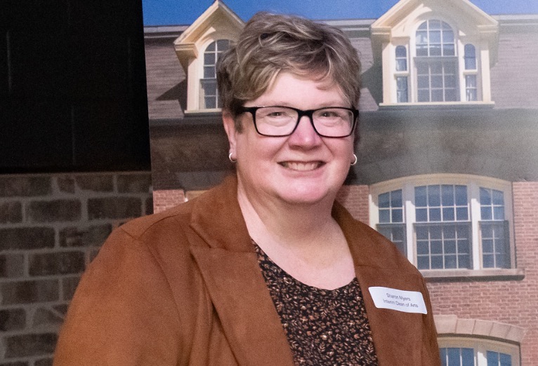 photo of woman wearing glasses standing near a backdrop