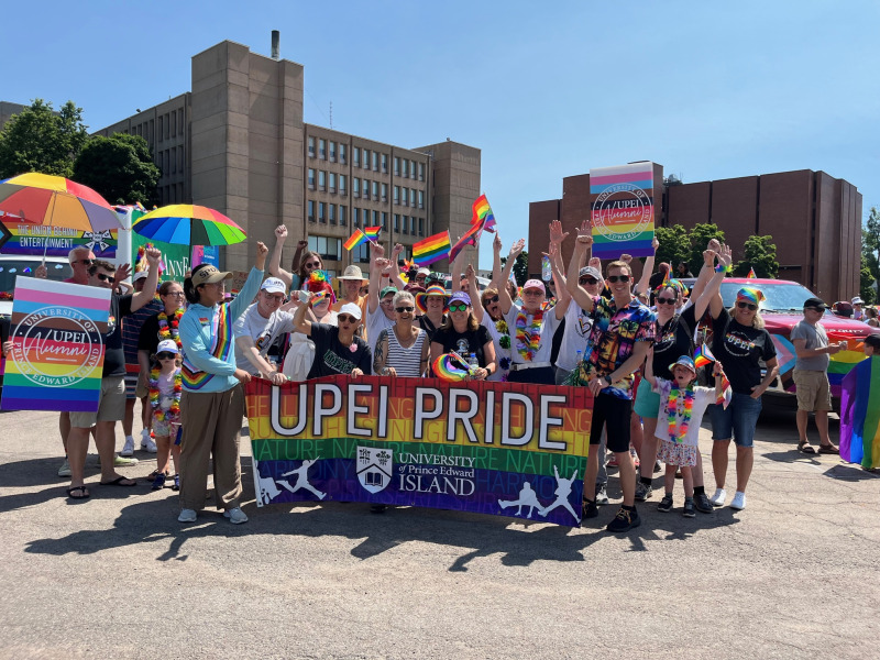 Photo of large group of people holding a banner and wearing clothing in bright rainbow colours