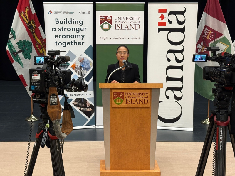 Dr. Beibei Jia, Assistant Professor, Epidemiology, AVC, speaks at the news conference announcing funding for shellfish health research and resilience projects. Photo of a woman standing at a podium flanked by video cameras