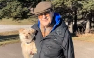 Photo of man standing outside holding a small dog