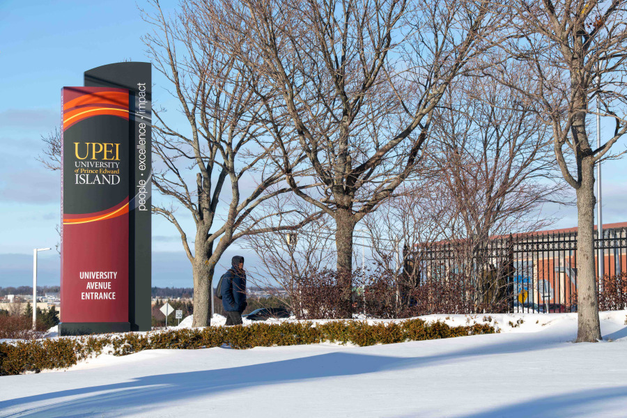 Student walking by sign at the entrance of University in winter