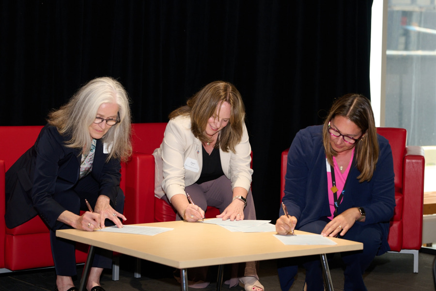 Photo of three people gathered around a table, each signing a document