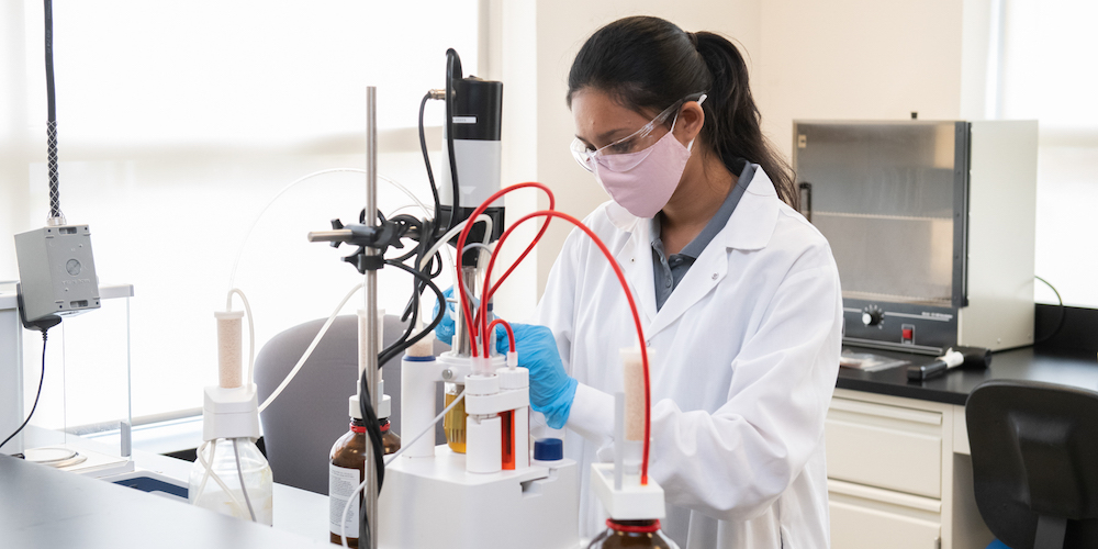 female student wearing a non-medical mask and protective glasses working in a laboratory