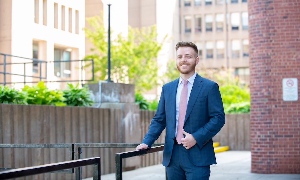 a UPEI graduate in a blue suit outside PEI's government buildings