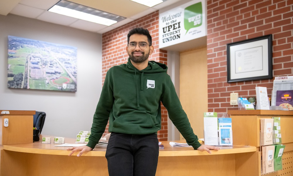 a UPEI student in a green UPEISU hoodie standing in an office