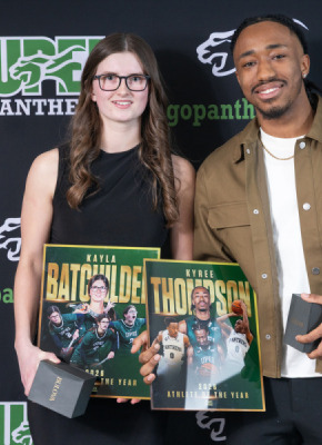 Photo of woman and man holding trophies in front of a backdrop
