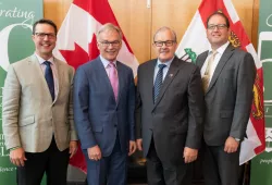 Four men stand before the Canada and PEI flags