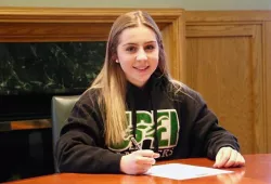 A smiling student signs a piece of paper