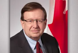 A portrait of an older man in front of a Canadian flag