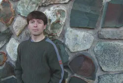 A man stands against a stone wall