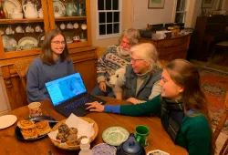 Two female students and a male and female farmer sit around a farmhouse table