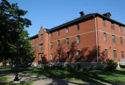 A brick building with shadows of leaves on the front on a sunny day