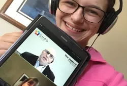 A young female holds up a digital tablet with the faces of a man and a woman on it