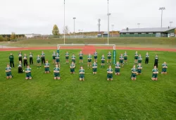 A group of female ruby players stand on a grass sports field