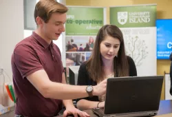 A male career counsellor points to a laptop screen of a female in a room marked "Career Stuido"