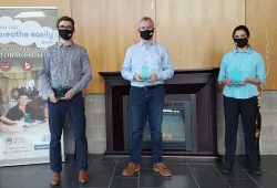 Two men and a woman stand in a line, spaced out for social distancing, wearing masks. 