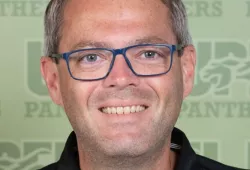 A smiling headshot of a man in glasses imposed over a a stylized UPEI Panthers background