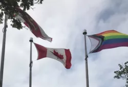 Photo of PEI, Canada and Progress Pride flags flying on poles on the UPEI campus