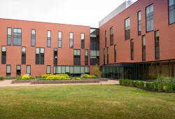 A modern-looking red brick building, three stories with two prominent wings. A landscaped garden with sitting space on benches in the foreground. 