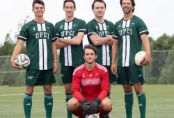 A squad of male soccer players pose for the camera with goalie kneeling in the foreground