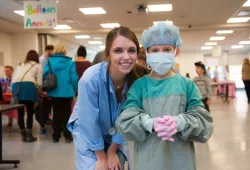 An AVC student helps an attendee get gowned and gloved like a surgeon.