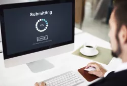 Photo of man sitting at a desk in front of a computer submitting an online form