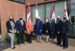 A group photo of men and women standing in front of an array of flags from PEI and Canada