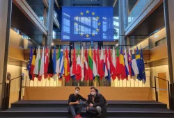 Image of two men sitting on steps in front of a group of flags