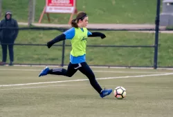 Woman dribbling soccer ball on grass pitch