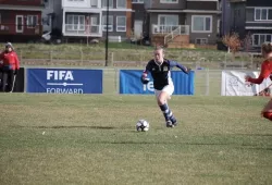 photo of woman dribbling soccer ball on a grass pitch