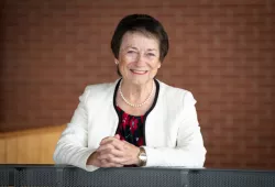 Photo of woman smiling leaning against railing with hands clasped