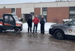 photo of three people standing between two vehicles in front of a brick building