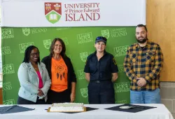 photo of four people standing behind a table with a cake and documents on it
