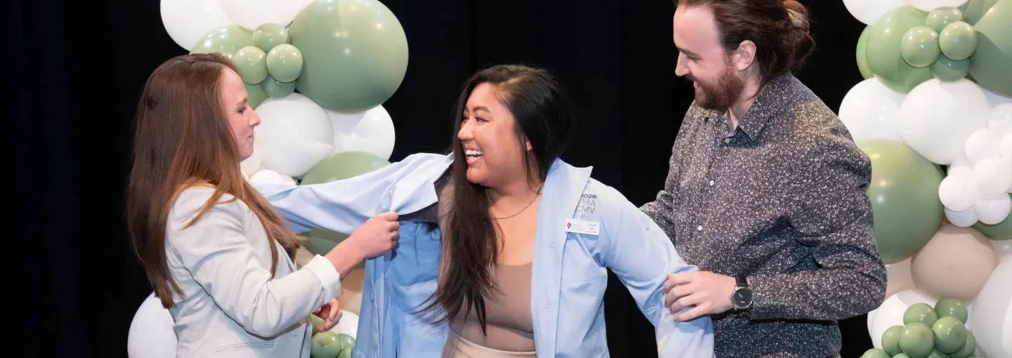 two people helping another person put on a blue lab coat