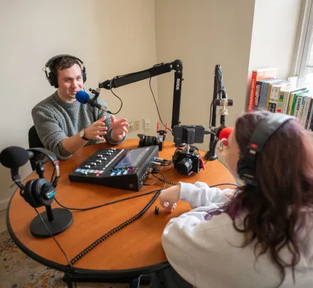 two students wearing headphones while speaking into microphones