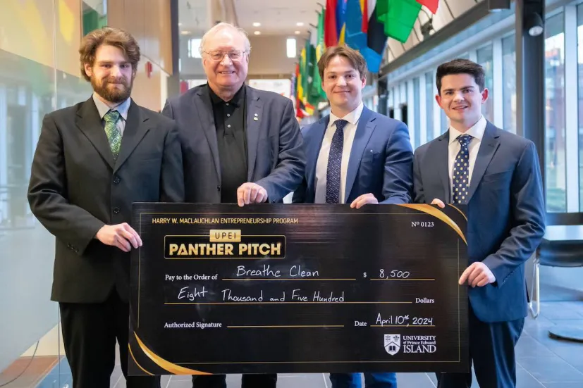 a group of three student entrepreneurs and a donor holding a large check