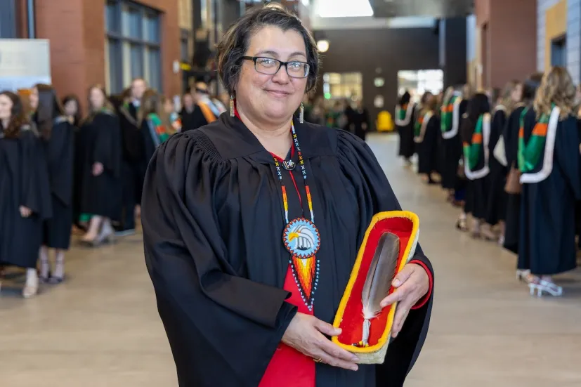 a faculty member in a black gown holding an eagle feather