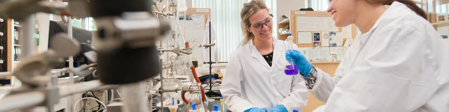 two chemistry students in laboratory with coloured flasks 