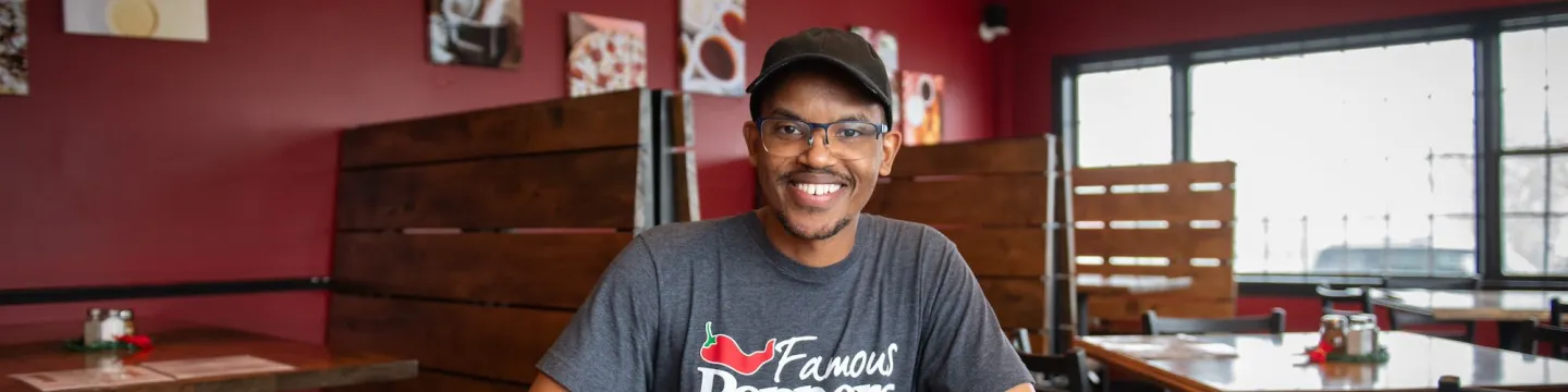 a smiling man sitting at a restaurant table writing on a clipboard